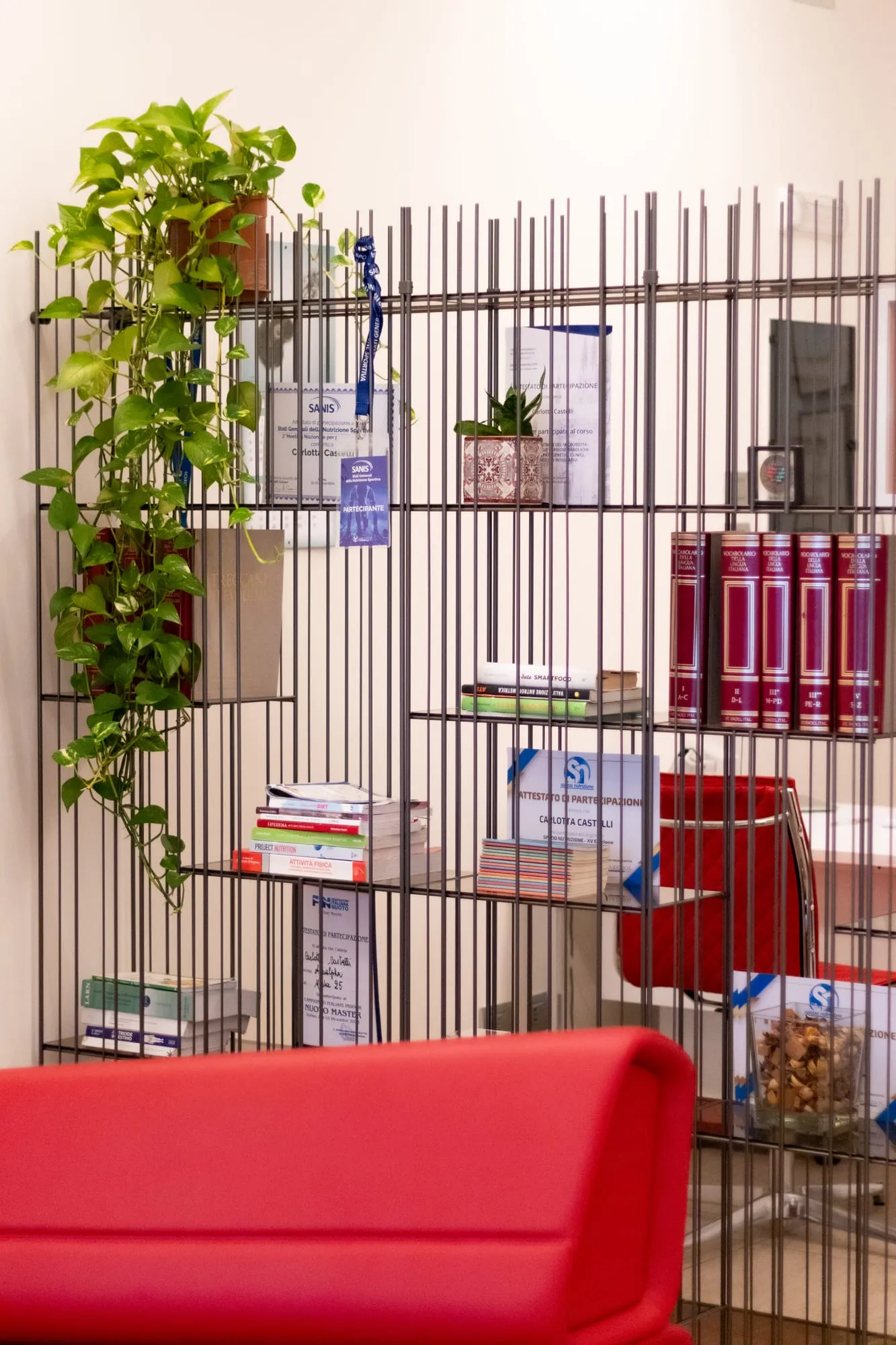 La libreria con le piante e il divano rosso dello studio di Melzo